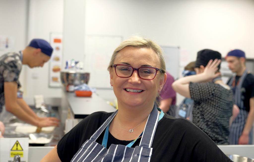 Female Wirral Met Hospitality and Catering student smiling wearing a grey and white striped apron